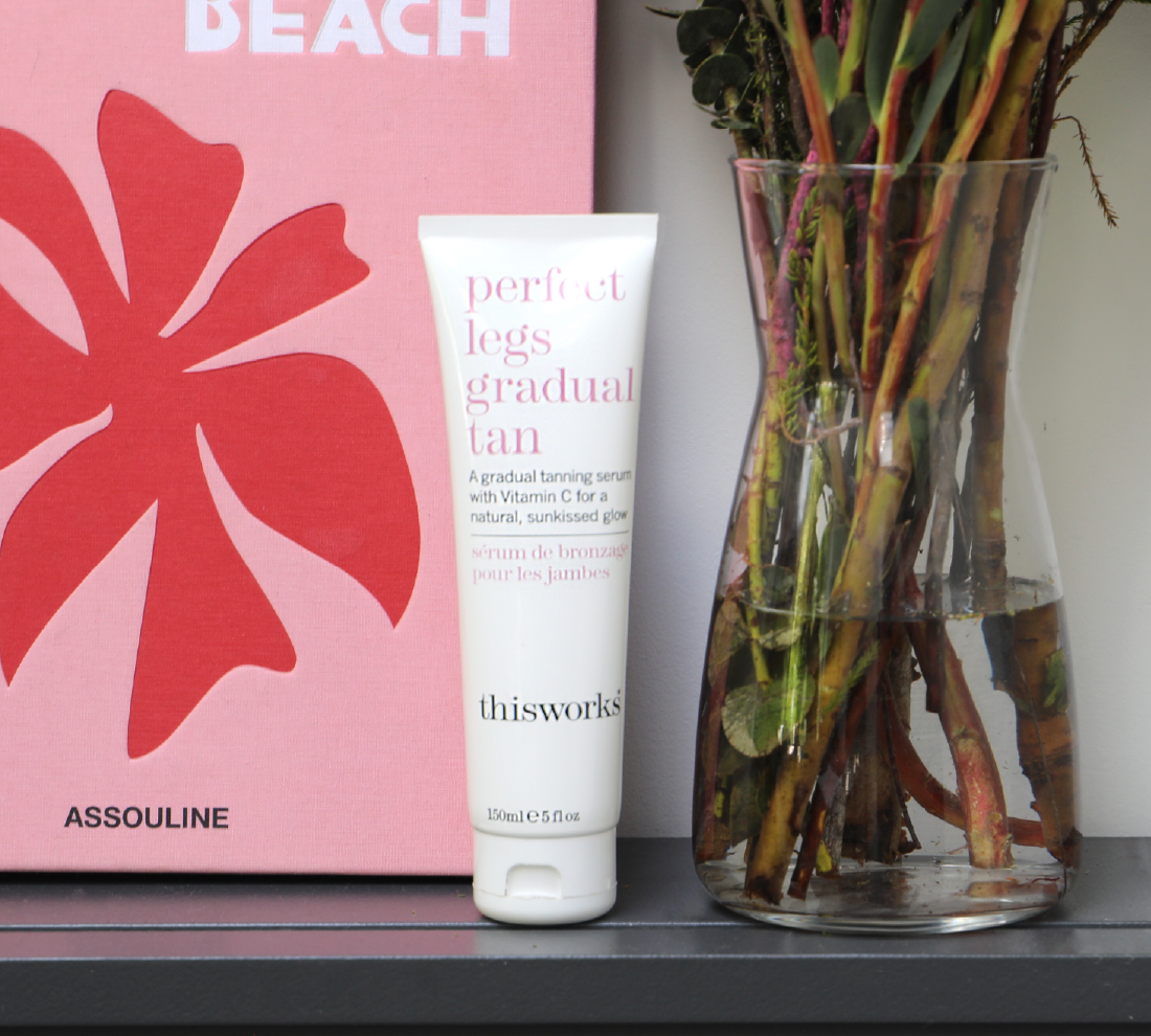 A white tube of thisworks Perfect Legs Gradual Tan serum sits on a dark shelf