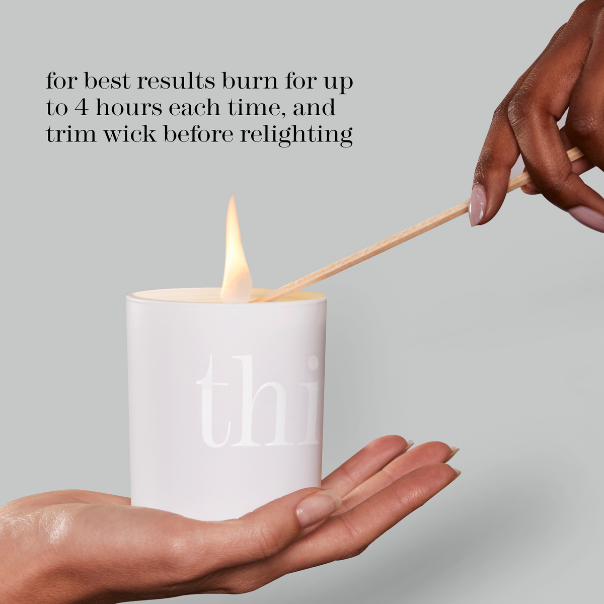 A white cylindrical candle with a visible flame is held in two hands, with a wooden matchstick resting across the top. Text on the image reads, 'for best results burn for up to 4 hours each time, and trim wick before relighting.